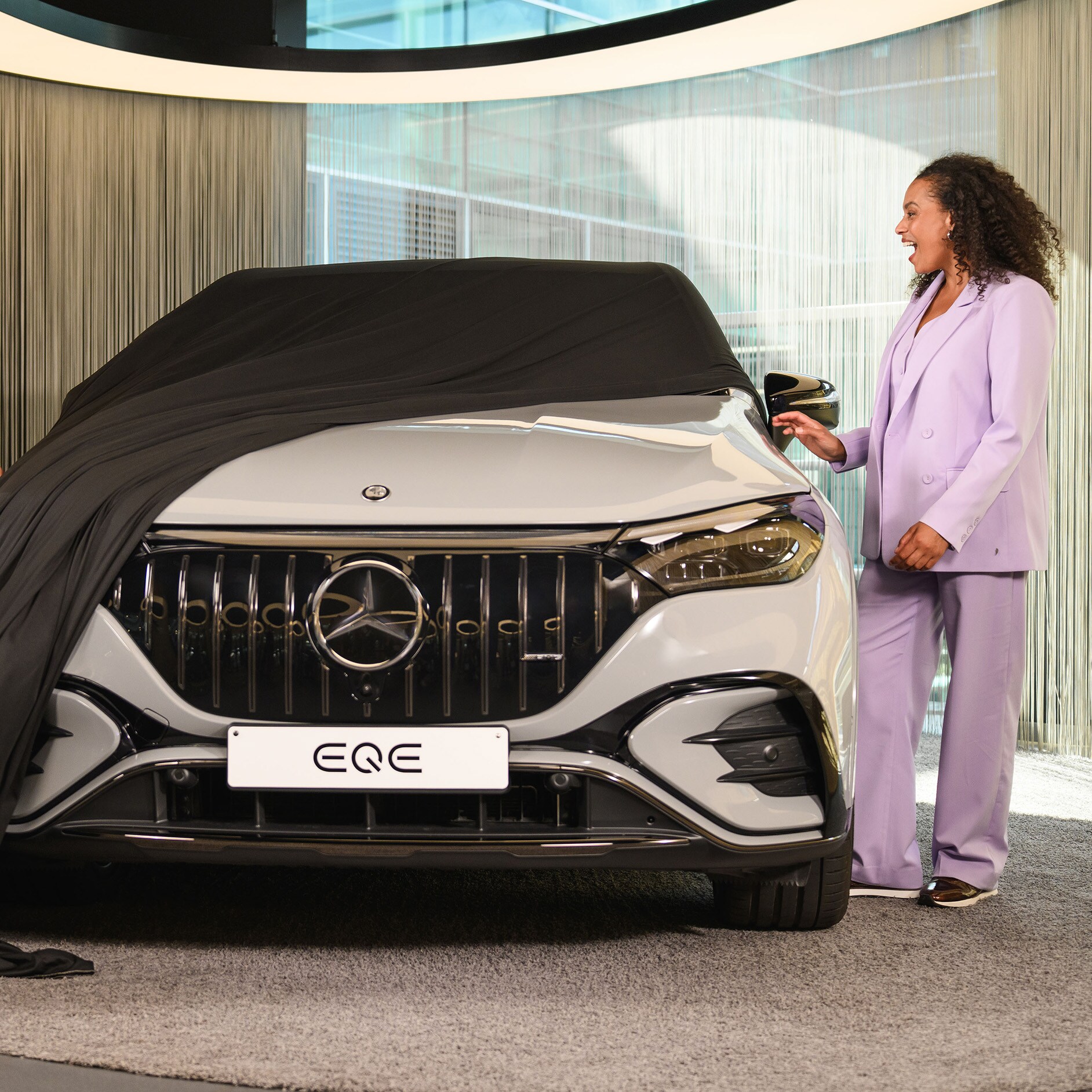 Financieringsaanbod voor uw nieuwe Mercedes-Benz Twee personen en een kind die de hoes van een nieuw Mercedes-Benz voertuig verwijderen in een showroom.