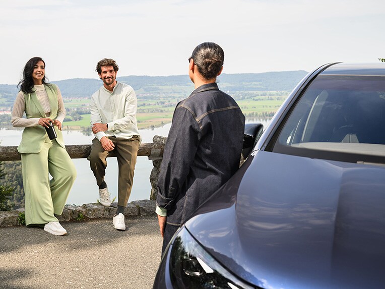 Verzekeringsdekking voor uw Mercedes-Benz | Mercedes-Benz autoverzekering Een persoon leunt tegen een Mercedes-Benz voertuig en praat met twee andere personen die tegen een hek leunen.