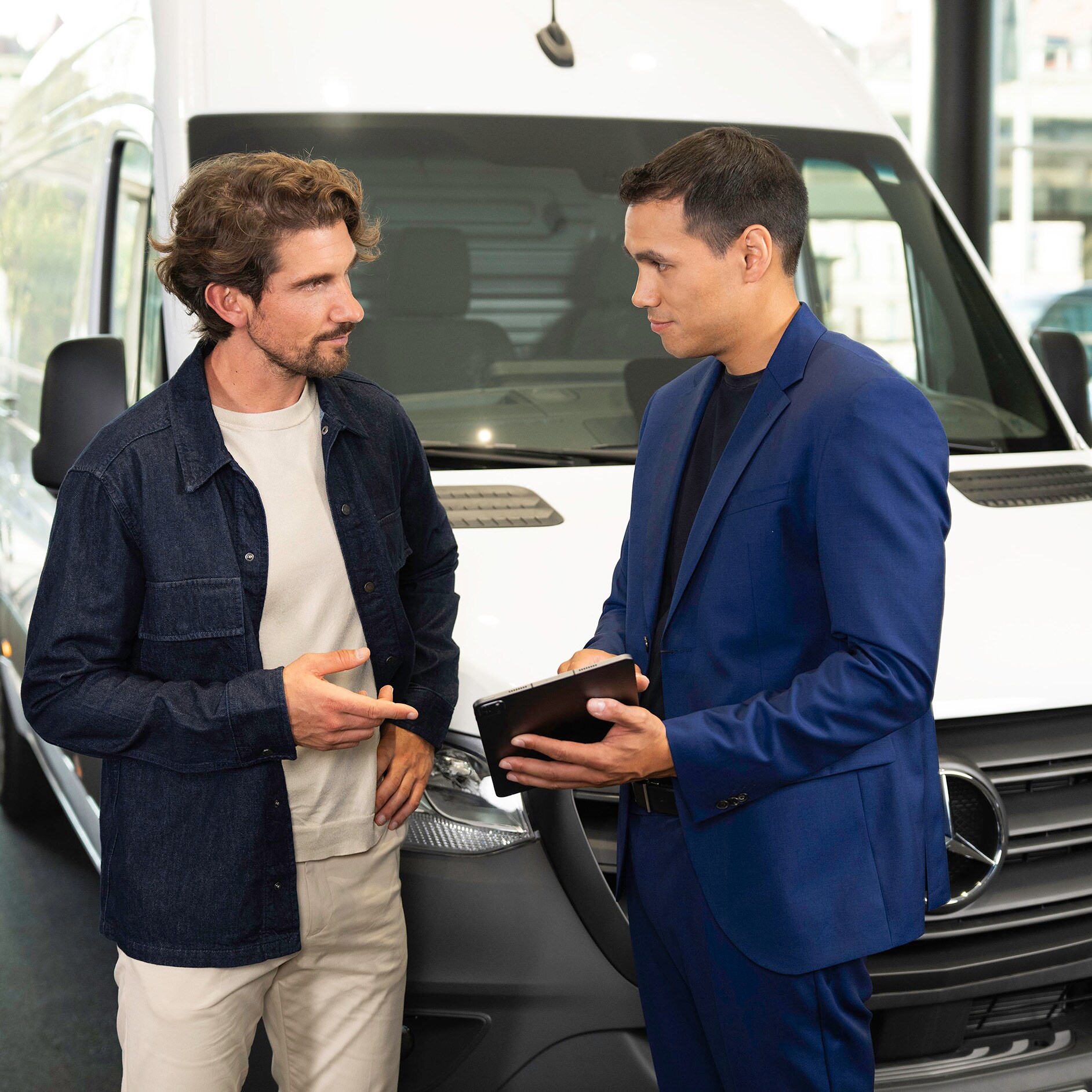 Décompte d’expertise Deux personnes discutent et pointent vers un appareil mobile tout en se tenant devant un utilitaire Mercedes-Benz.