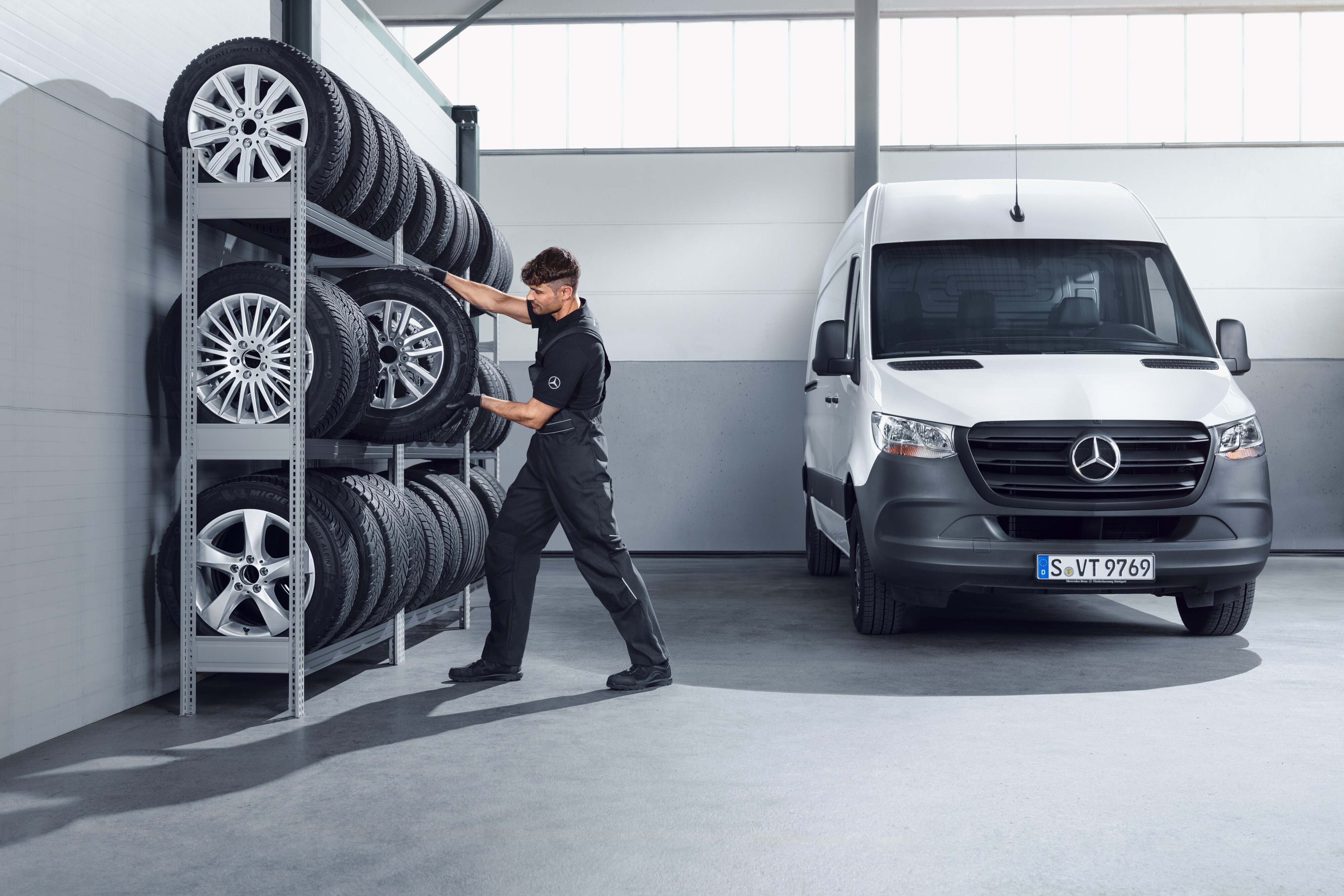 Mercedes-Benz | Pièces d'origine de qualité pour les utilitaires légers Mécanicien sélectionnant les roues d'hiver Mercedes-Benz complètes pour un Sprinter blanc sur l'étagère de l'atelier.